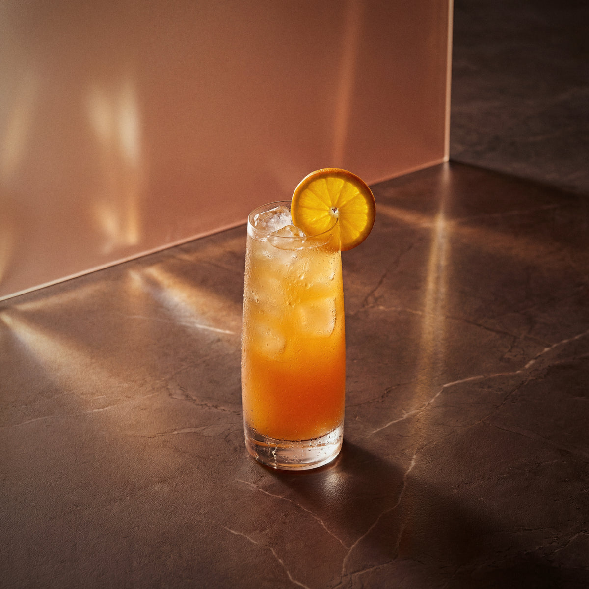 alabama slammer cocktail with amaretto liqueur in a highball glass with a orange wheel on a textured surface 