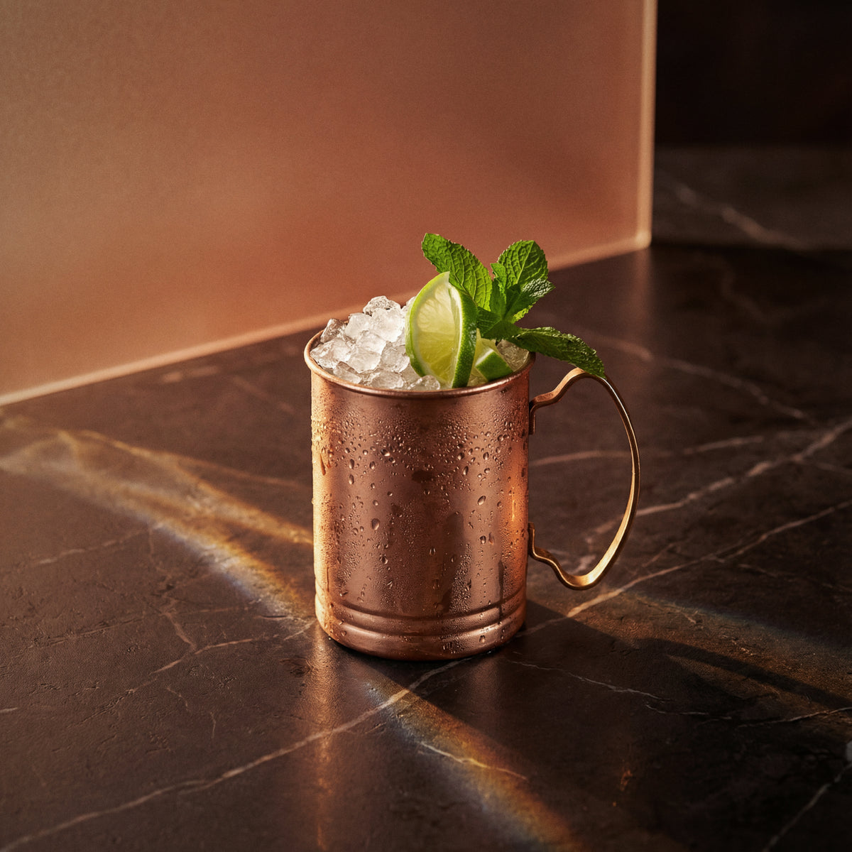 copper mug with a amaretto mule cocktail garnished with lime and mint leaves on a dark marble surface.