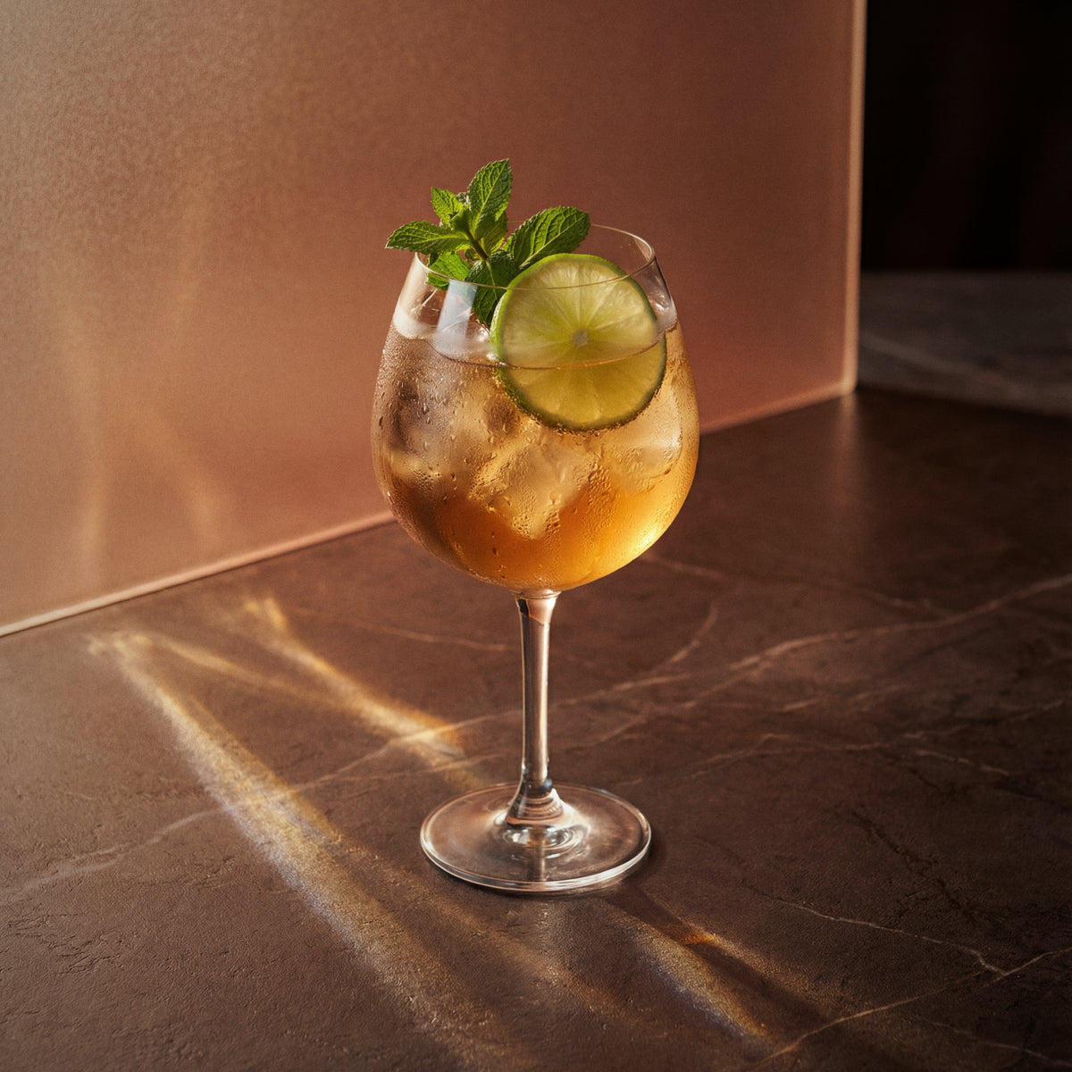 amaretto spritz cocktail with amaretto liqueur in a coppa glass with lime wheels and mint sprigs on a marble surface
