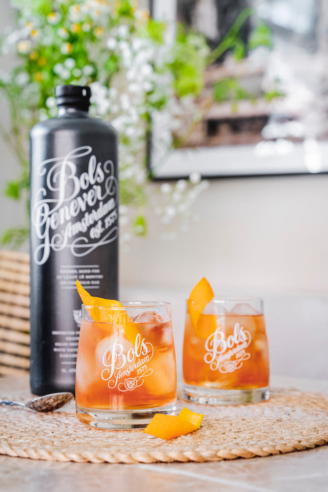 Two glasses of negroni cocktail with 'Bols Barrel aged Genever' branding on a woven mat.
