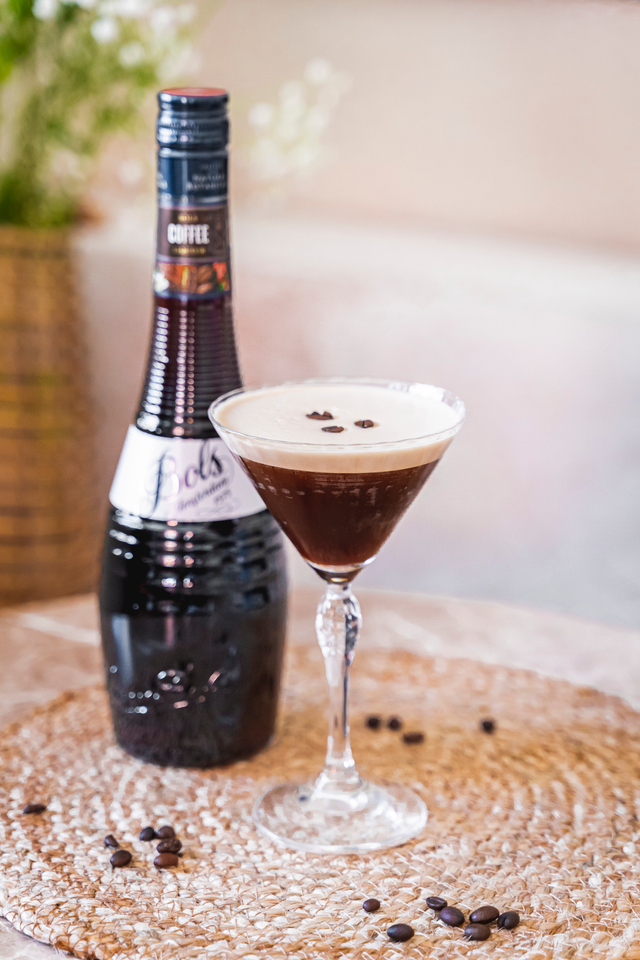 Bottle of coffee liqueur next to a cocktail glass with coffee liqueur on a textured surface.