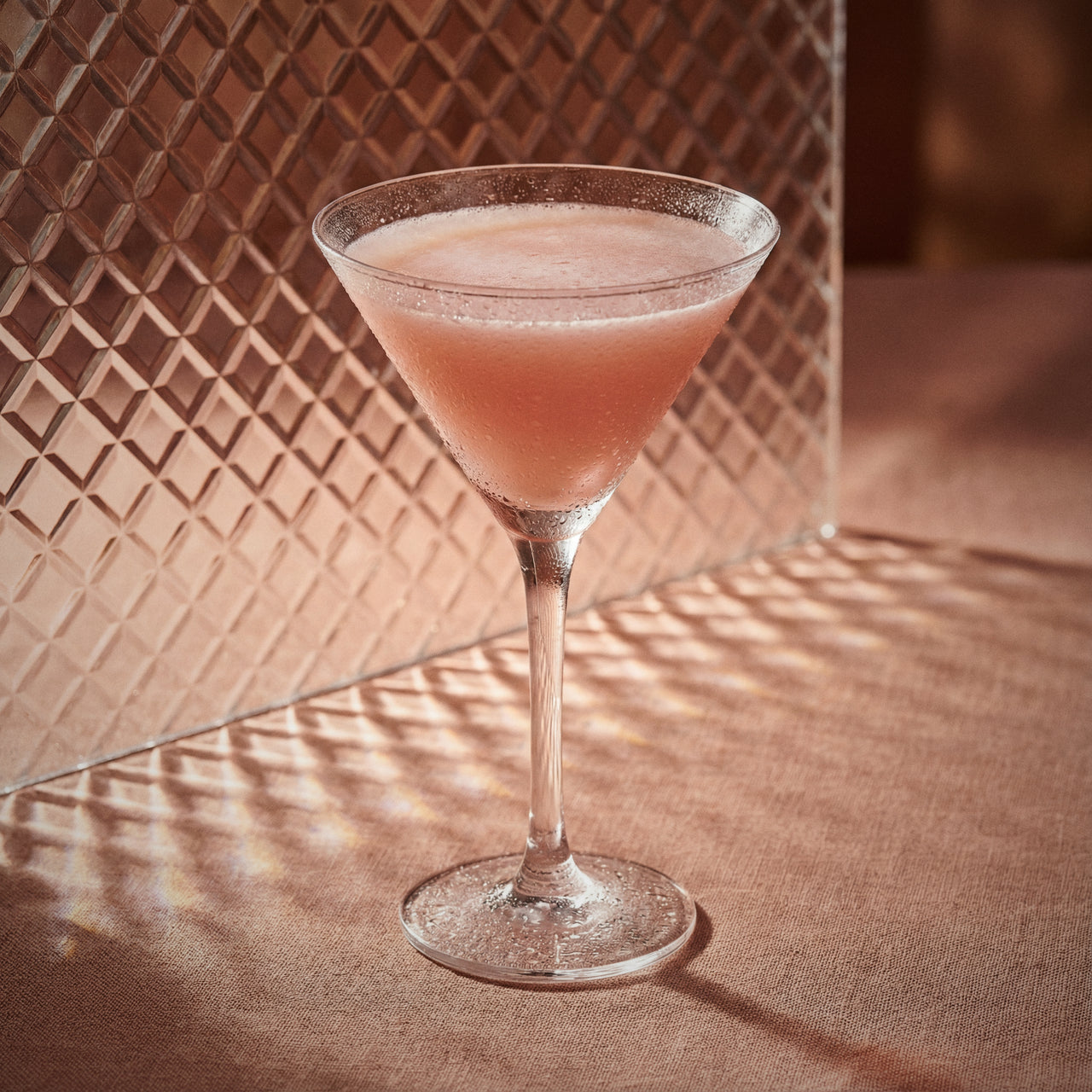 chocolate pumpkin cocktail in a martini glass with cacao white liqueur and pumpkin spice liqueur on a textured surface with a patterned wall in the background