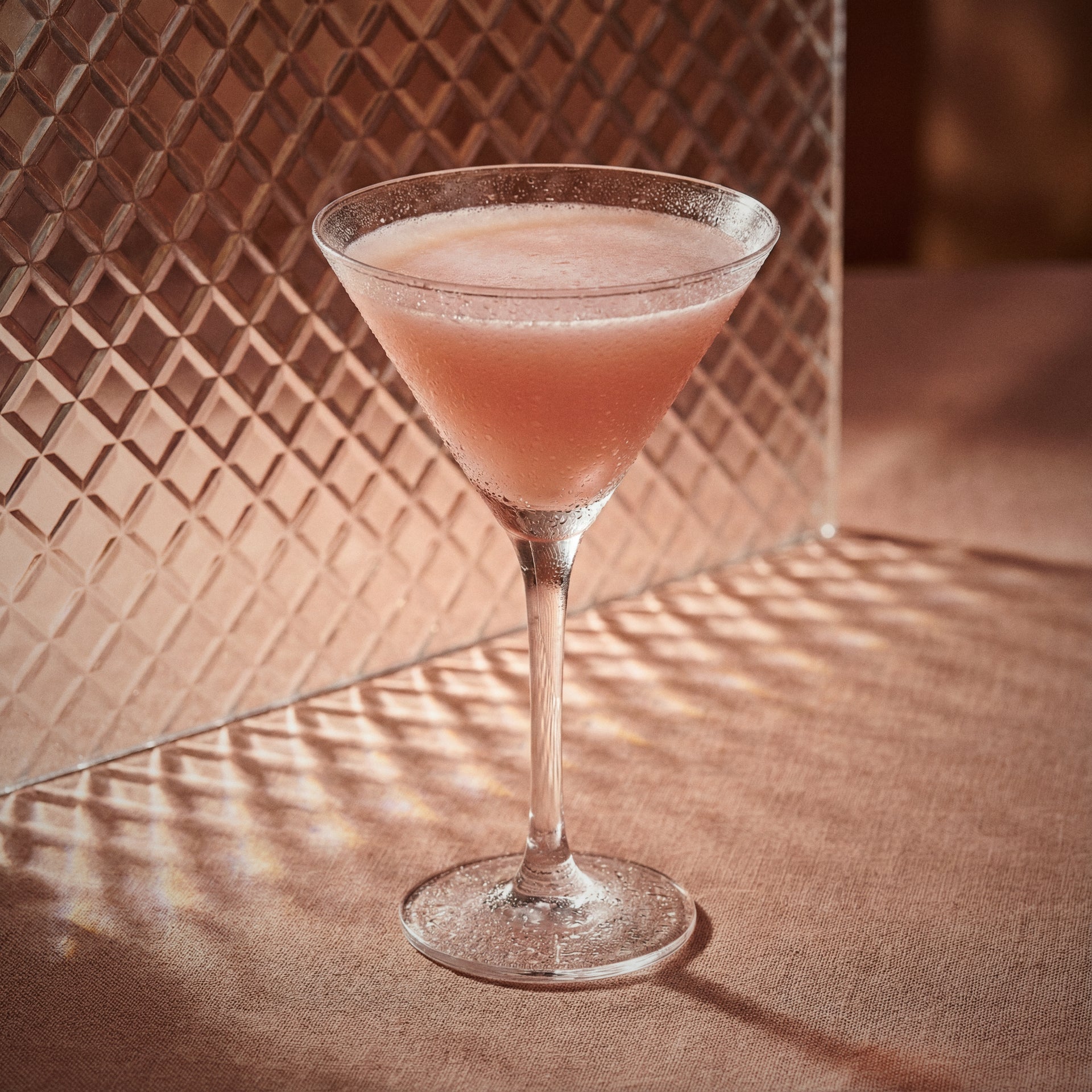 chocolate pumpkin cocktail in a martini glass with cacao white liqueur and pumpkin spice liqueur on a textured surface with a patterned wall in the background