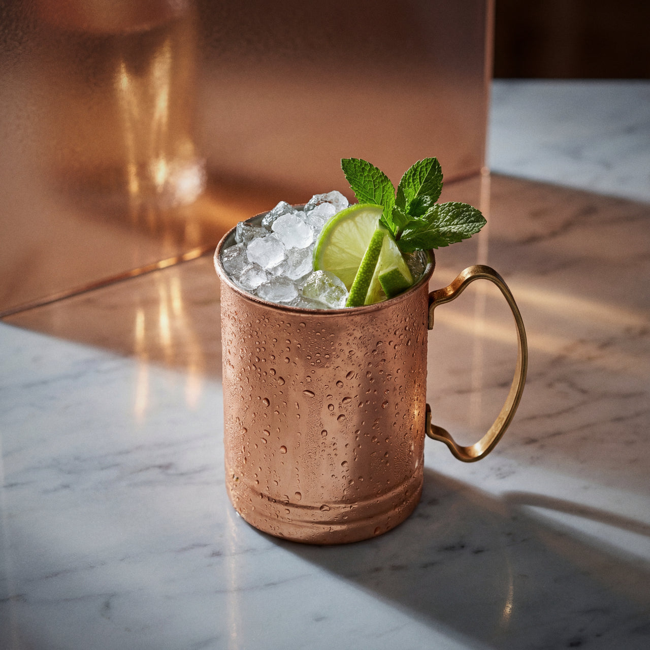coconut mule cocktail with coconut liqueur in a copper mug with lime wheels and mint on a textured surface