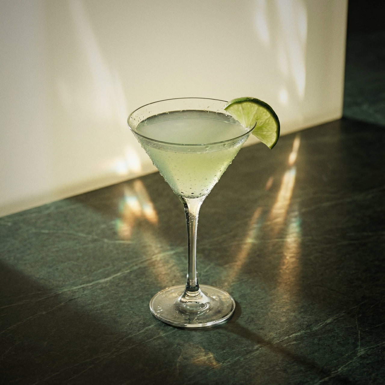 cucumber gimlet cocktail made with cucumber liqueur and gin in a martini glass and lime wedge on a textured surface