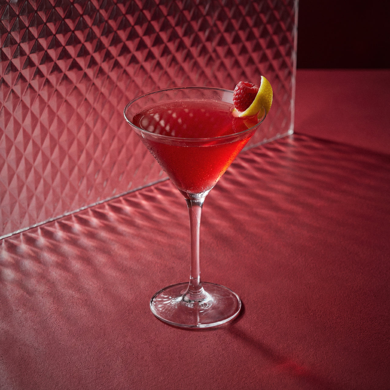 french martini cocktail with a raspberry and raspberry liqueur in a martini glass on a red surface with a textured red wall background.