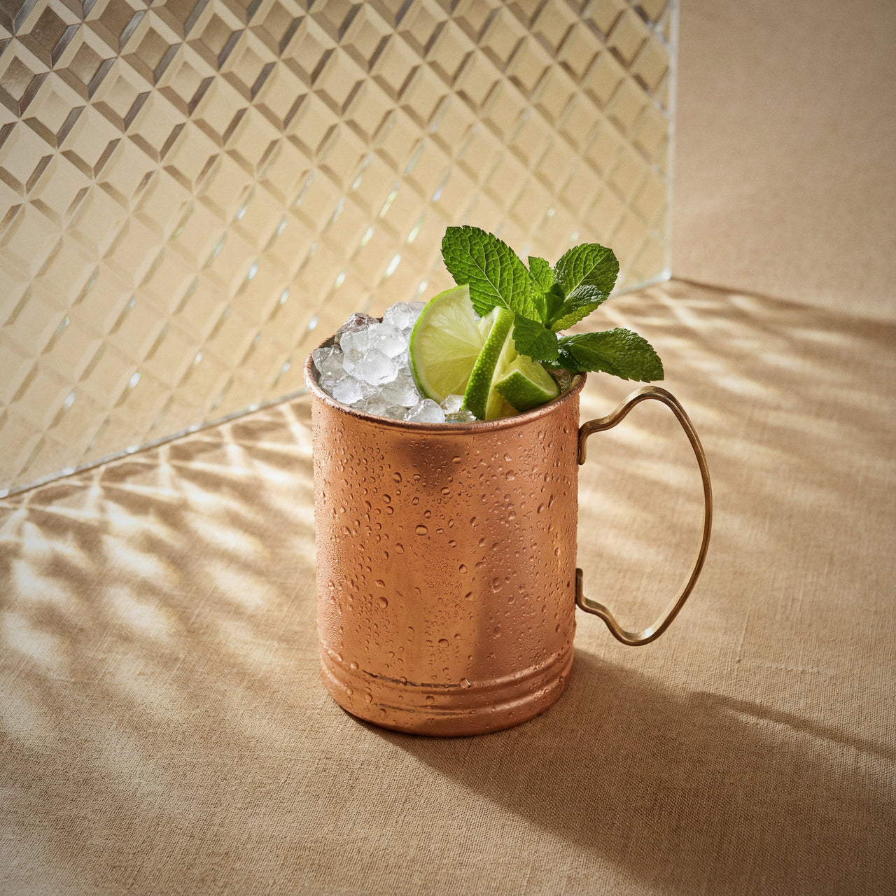 ginger mule cocktail in a copper mug, with ginger liqueur, lime wheel, and mint leaves on a textured surface.
