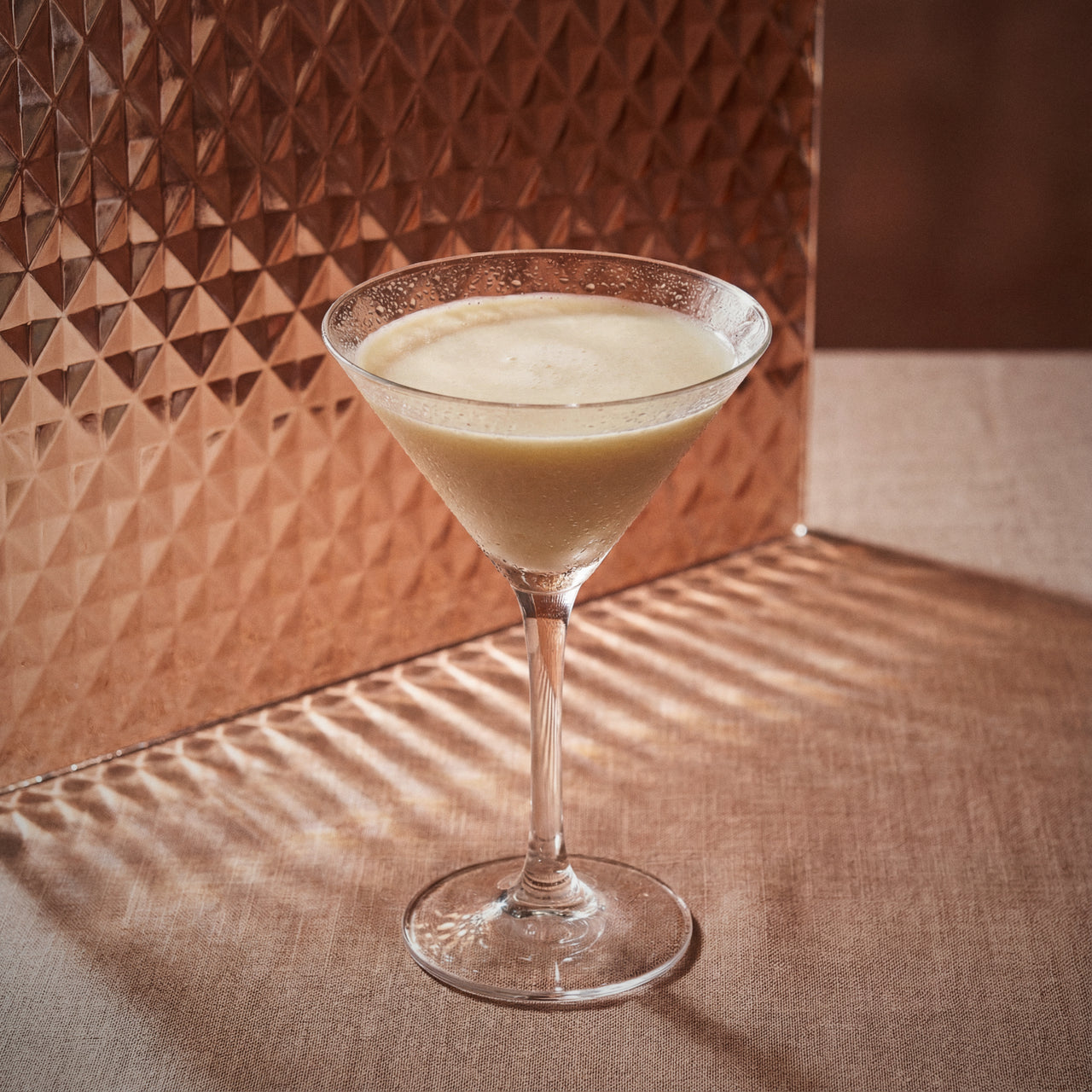 golden cadilac cocktail in a martini glass with cacao white liqueur on a textured surface with a geometric patterned wall in the background