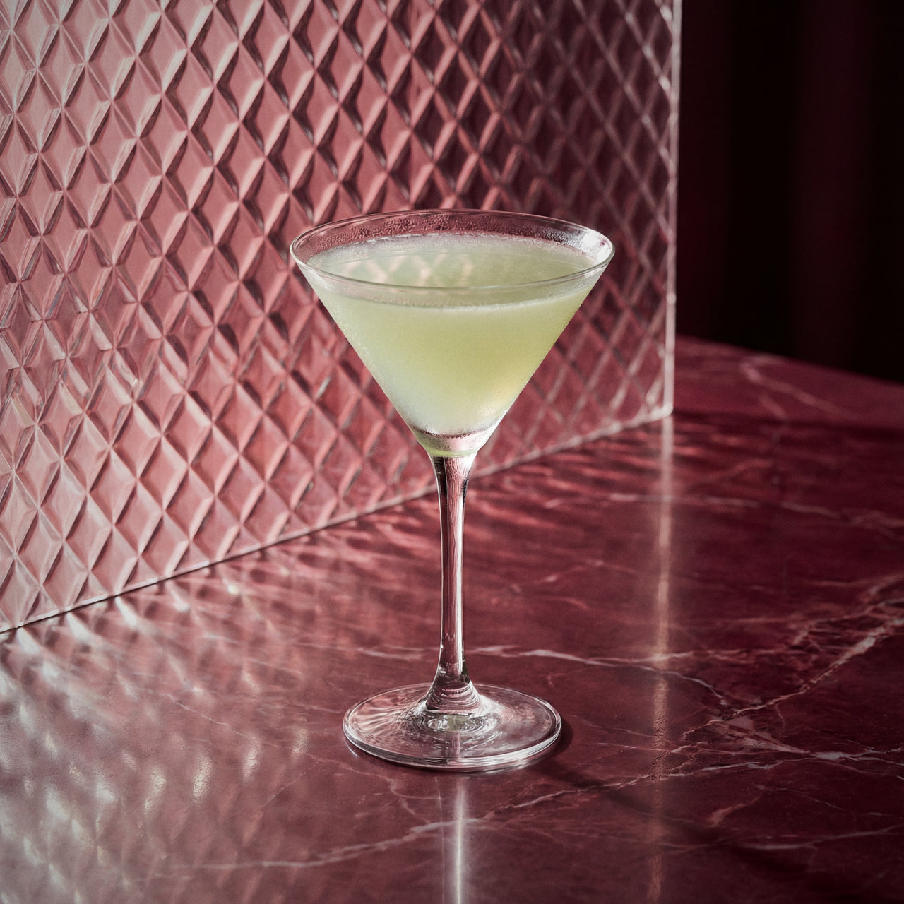 holland house cocktail in a martini glass with maraschino liqueur and genever on a textured red surface with a patterned wall in the background