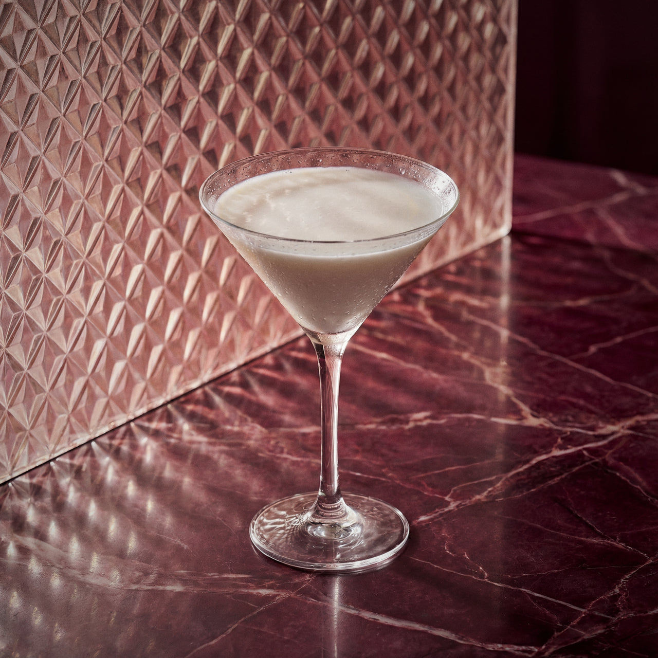 last word cocktail in a martini glass with maraschino liqueur and gin on a marble surface with a textured wall in the background