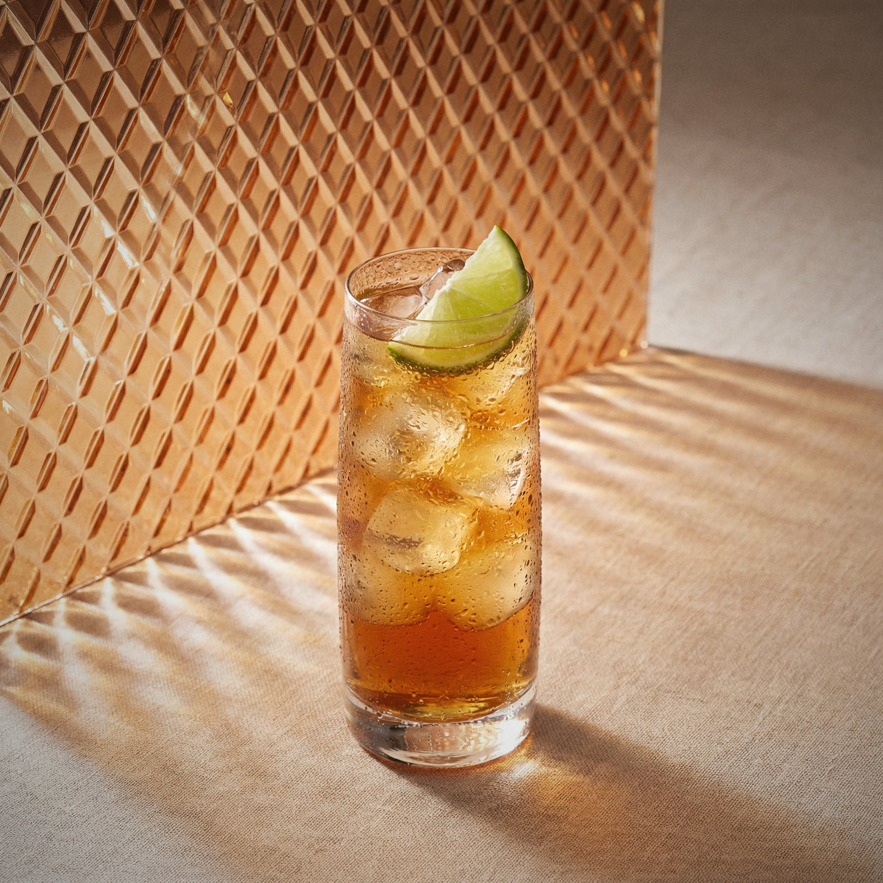 long island iced tea cocktail made with triple sec liqueur, gin, and vodka, with a lime wedge in a highball glass on a textured surface