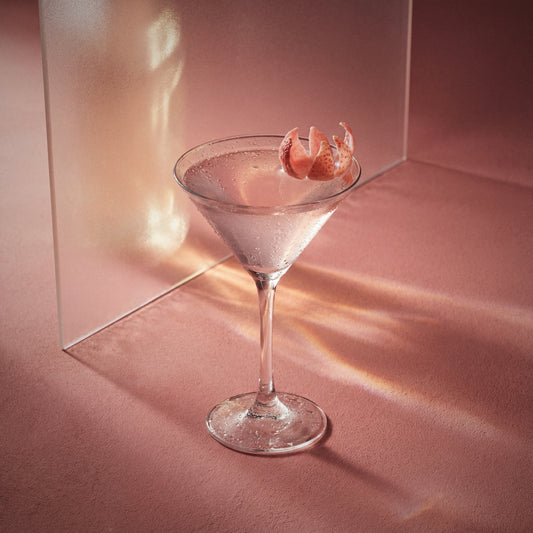 lychee martini cocktail in a martini glass with a lychee garnish on a pink background made with lychee liqueur and vodka