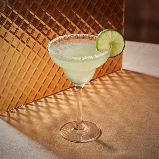 margarita cocktail with triple sec liqueur in a margarita glass with a lime wheel on a orange textured surface