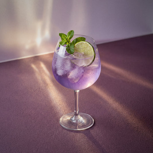 Purple parfait amour spritz cocktail with parfait amour liqueur and with lime and mint in a wine glass on a textured surface