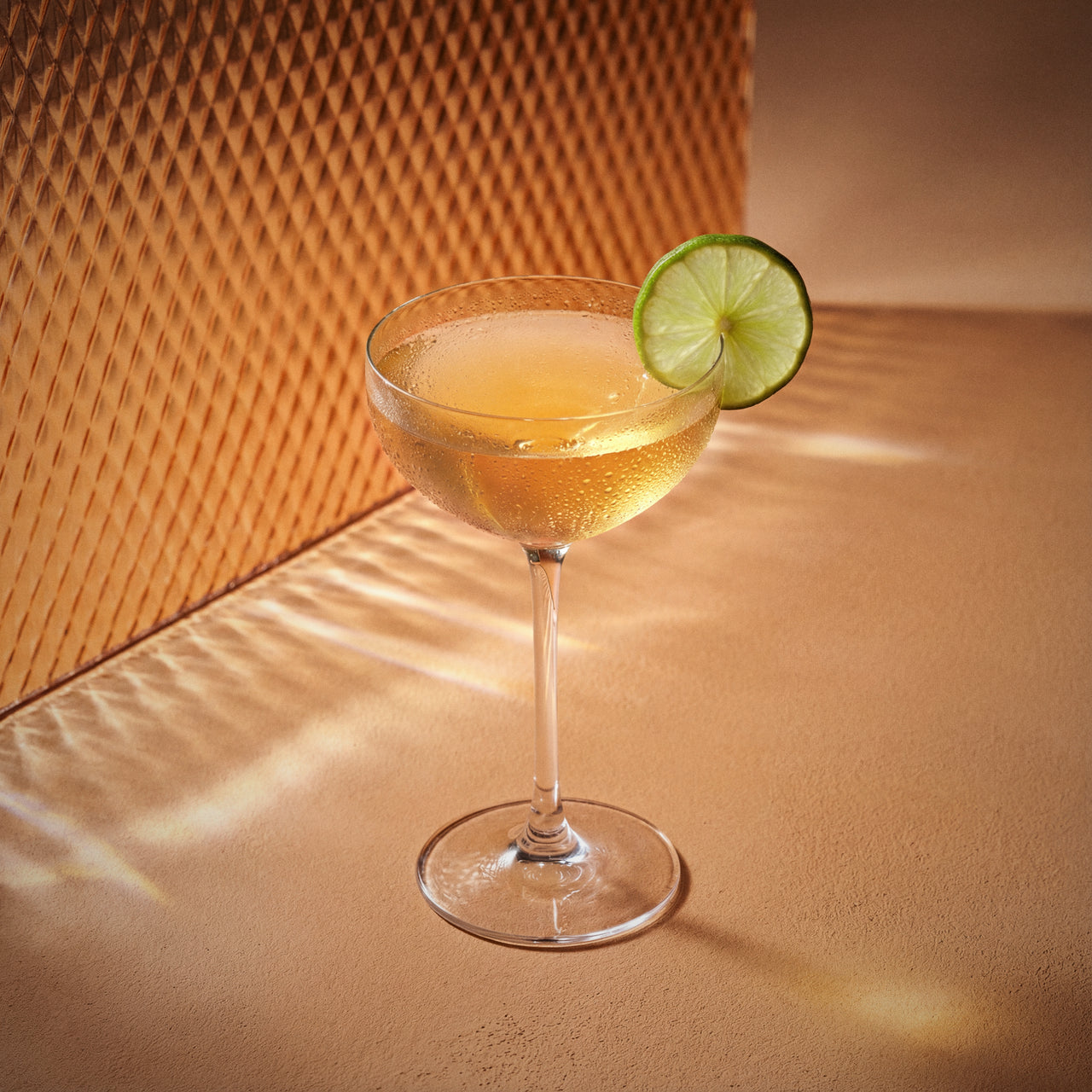 peach fizz cocktail in a coupe glass with peach liqueur and apricot brandy liqueur with a lime wheel on a textured surface
