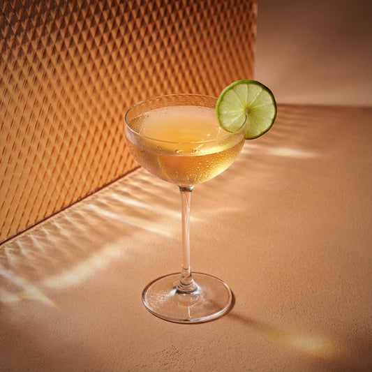 peach fizz cocktail in a coupe glass with peach liqueur and apricot brandy liqueur with a lime wheel on a textured surface