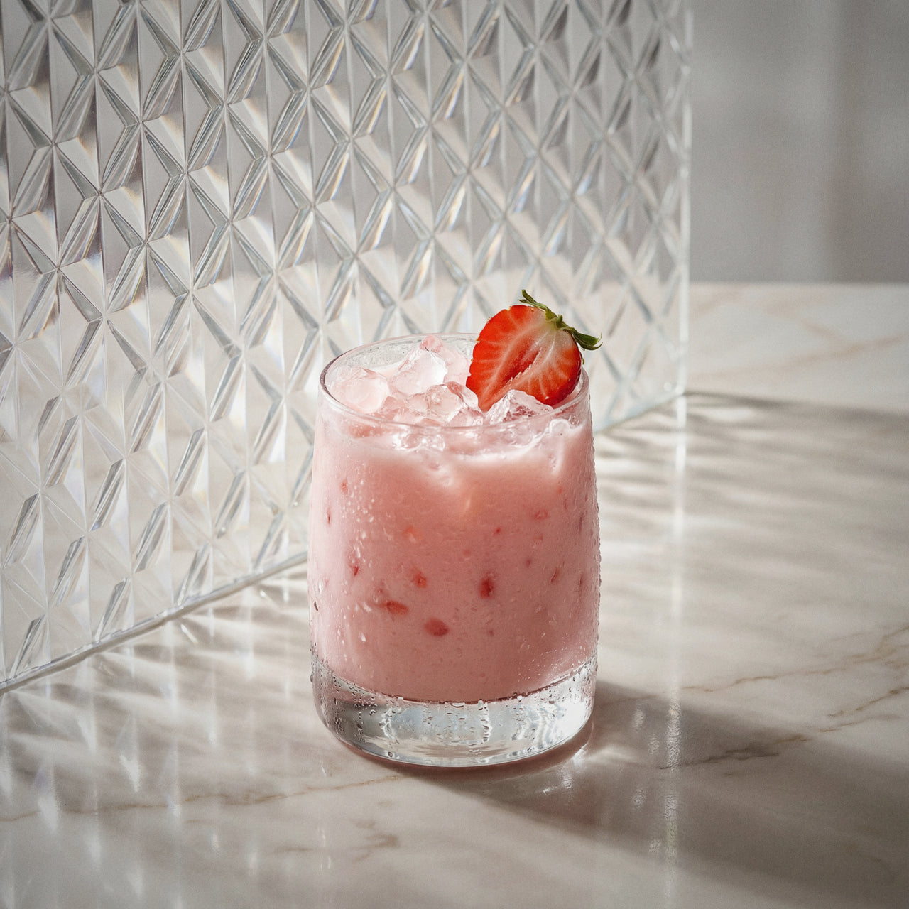 strawberry cheesecake cocktail with strawberry liqueur and natural yoghurt liqueur with a strawberry garnish on a marble surface