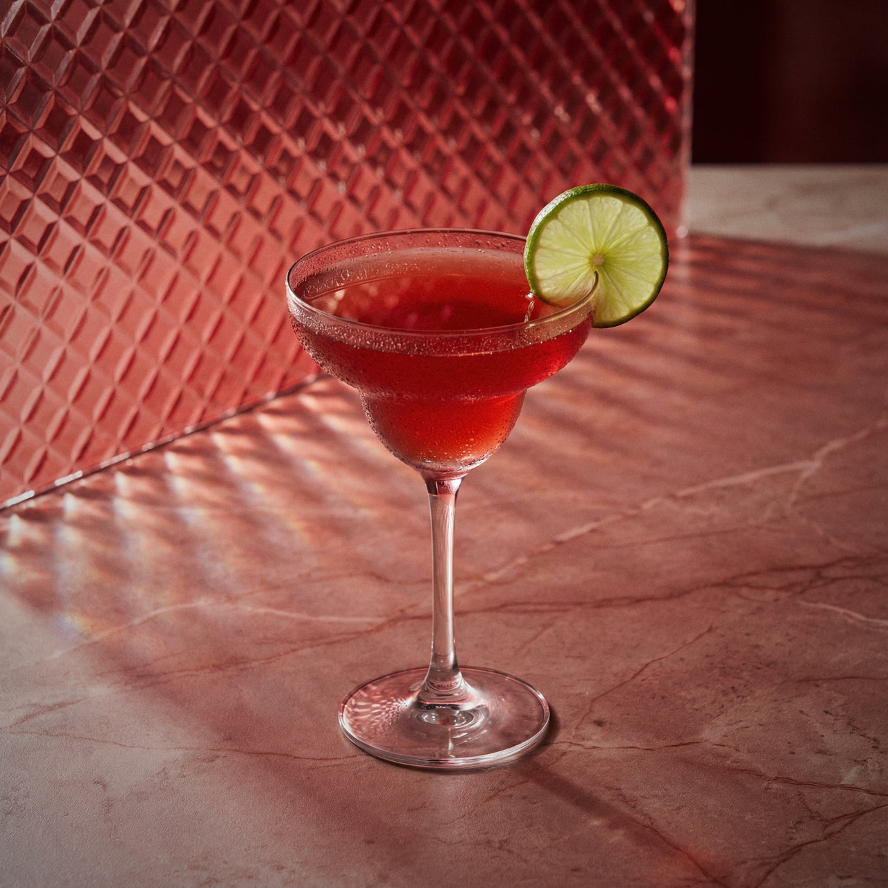 strawberry margarita cocktail with strawberry liqueur and a lime wedge in a margarita glass on a textured surface