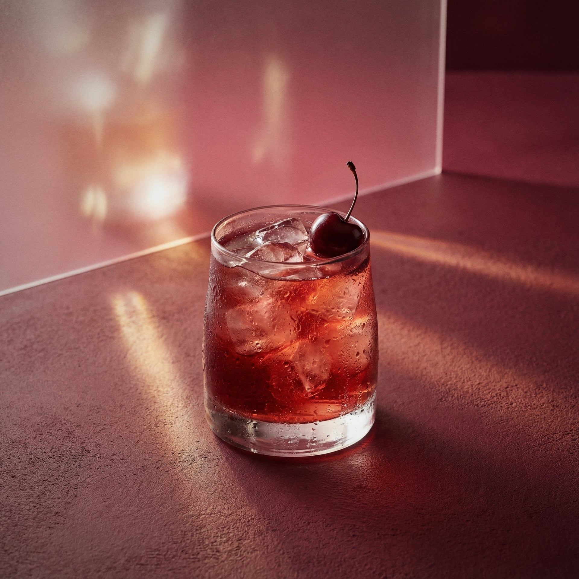 the rose cocktail with a cherry on a pink surface, with kirsche liqueur