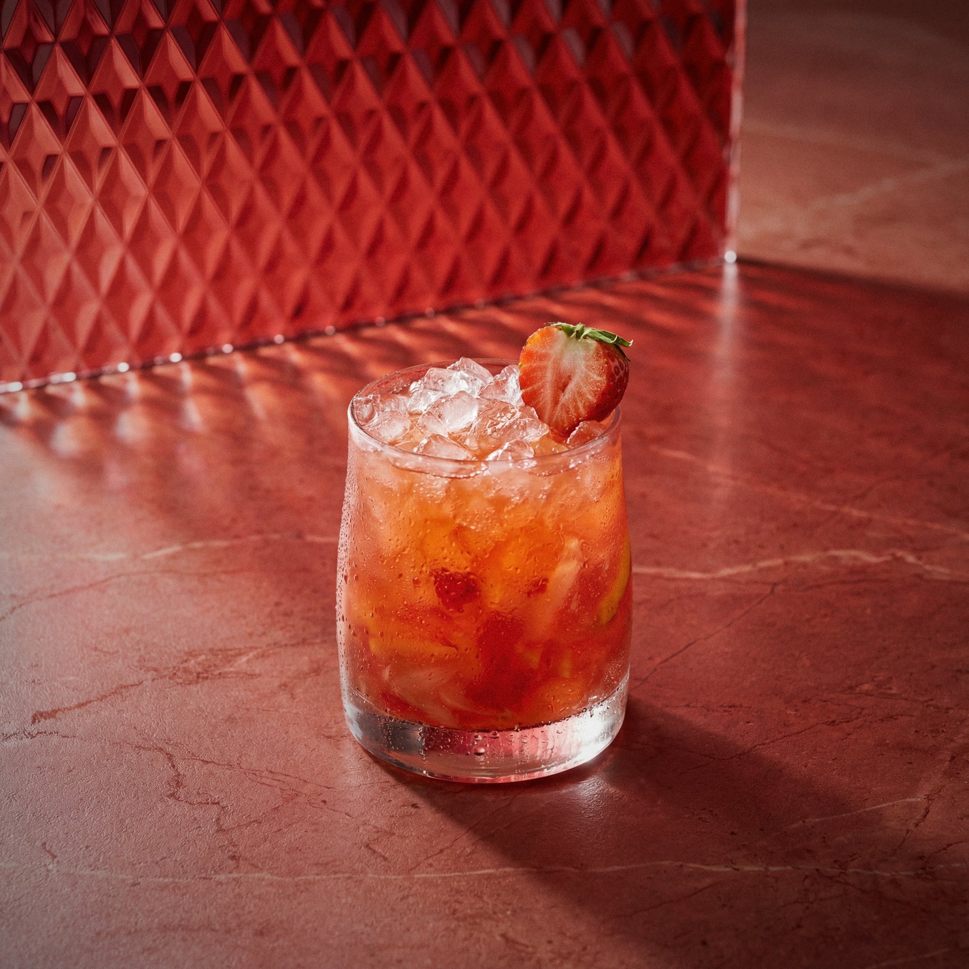 Vanilla Berry Crush cocktail with a strawberry garnish and strawberry liqueur and vanilla liqueur and genever 21 on a red textured surface