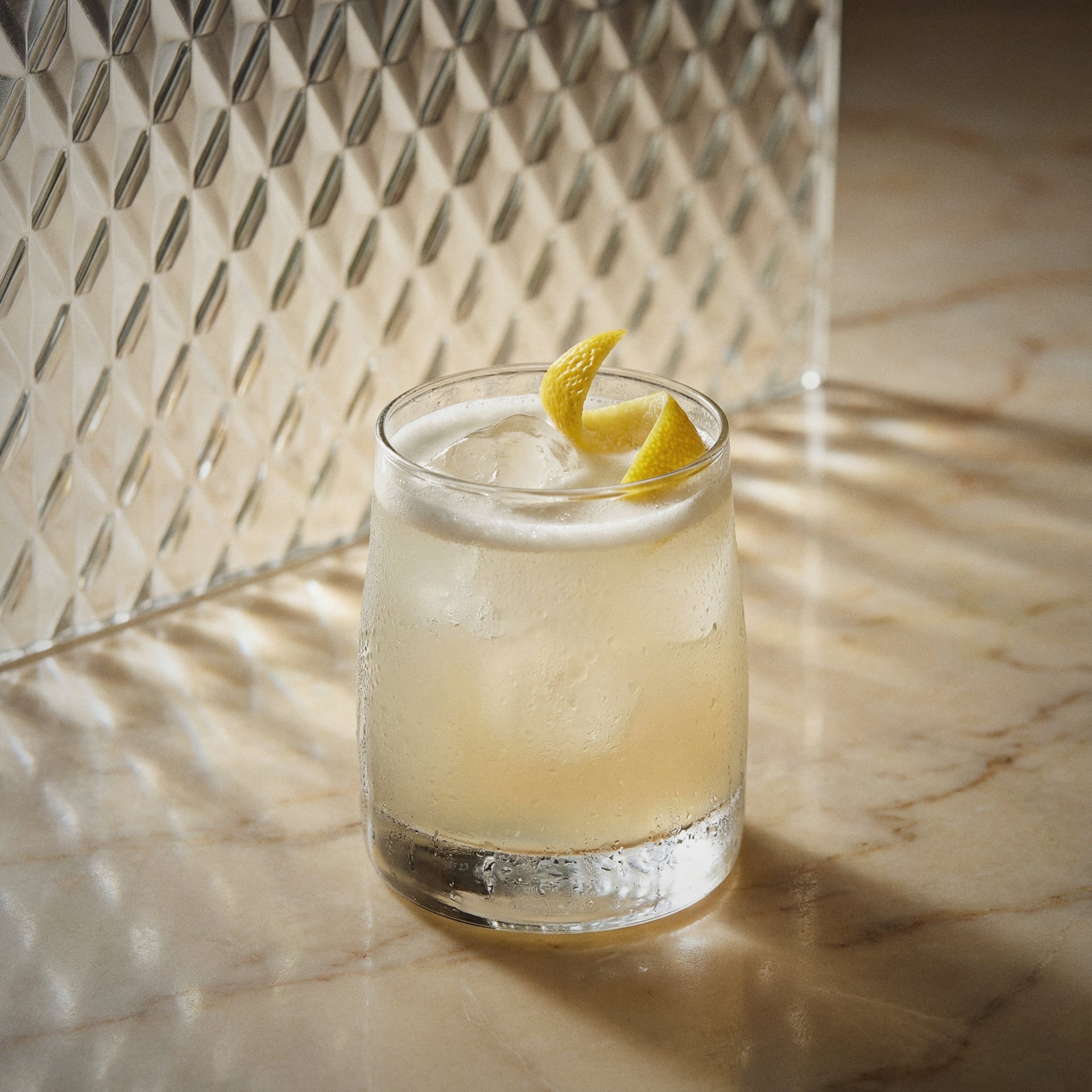 Vanilla sour cocktail with vanilla liqueur with a lemon twist on a marble surface with a textured wall background