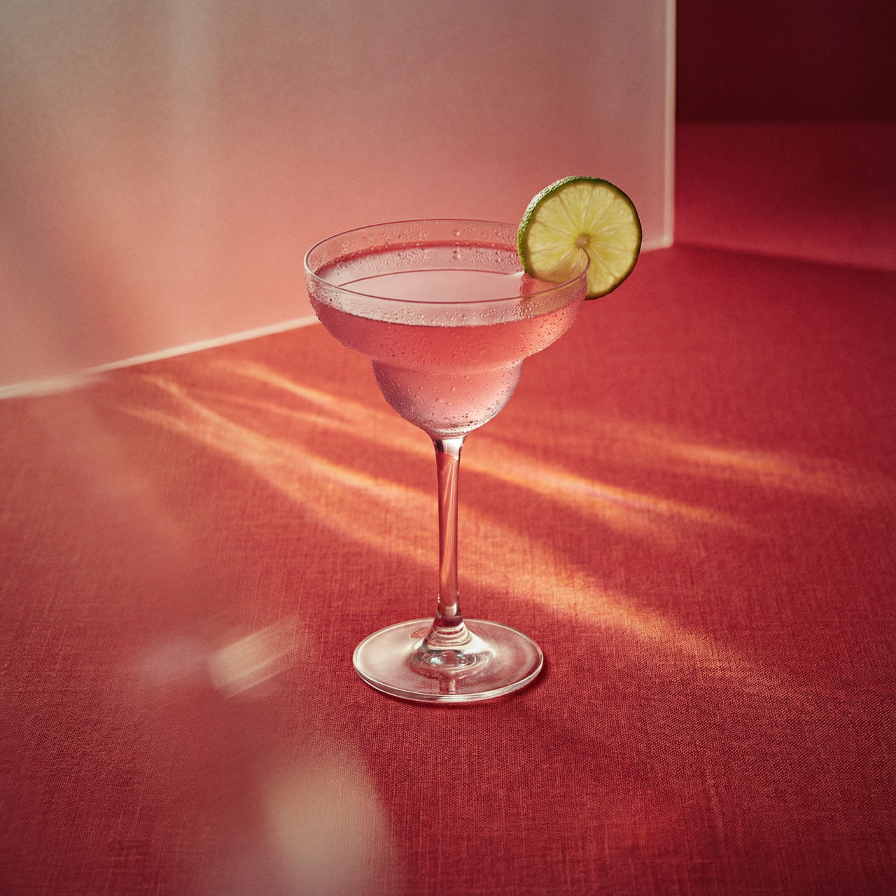 Watermelon margarita with watermelon liqueur, a pink cocktail with a lime wedge in a margarita glass on a red surface