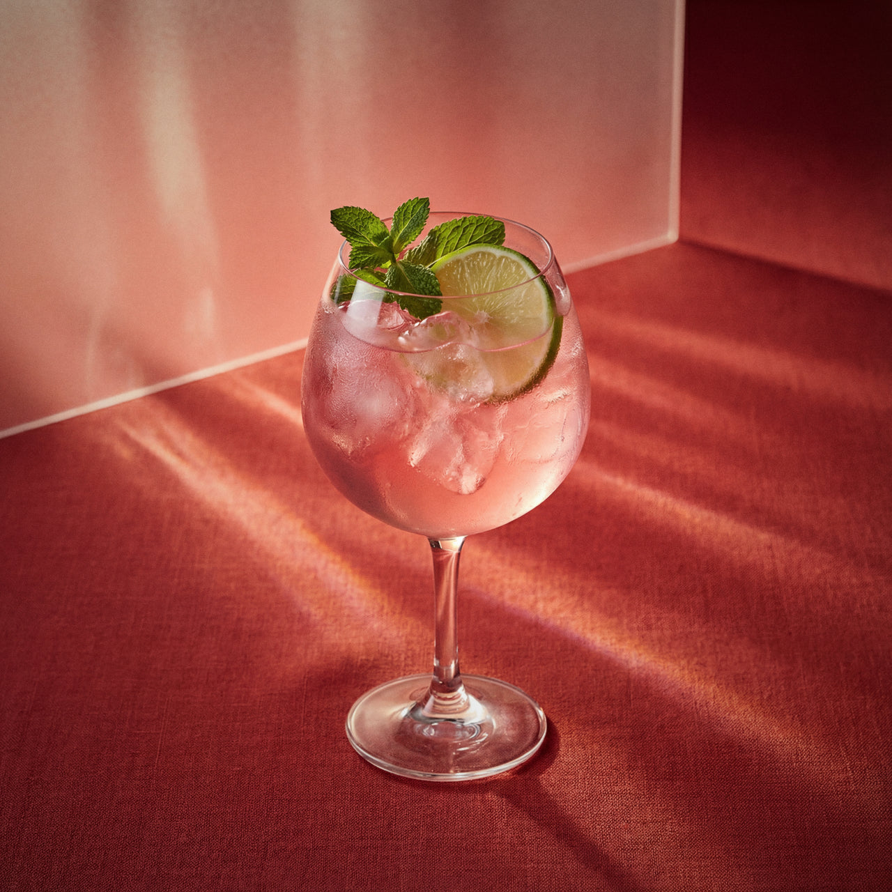 Watermelon Spritz cocktail with watermelon liqueur in a wine glass with lime and mint on a red surface