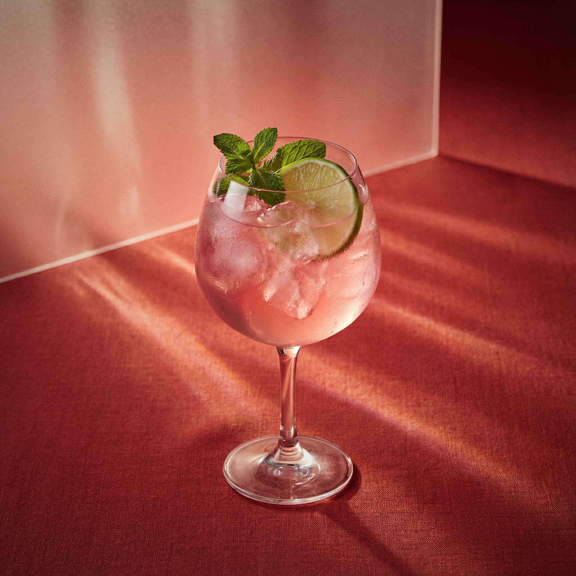 Watermelon Spritz cocktail with watermelon liqueur in a wine glass with lime and mint on a red surface