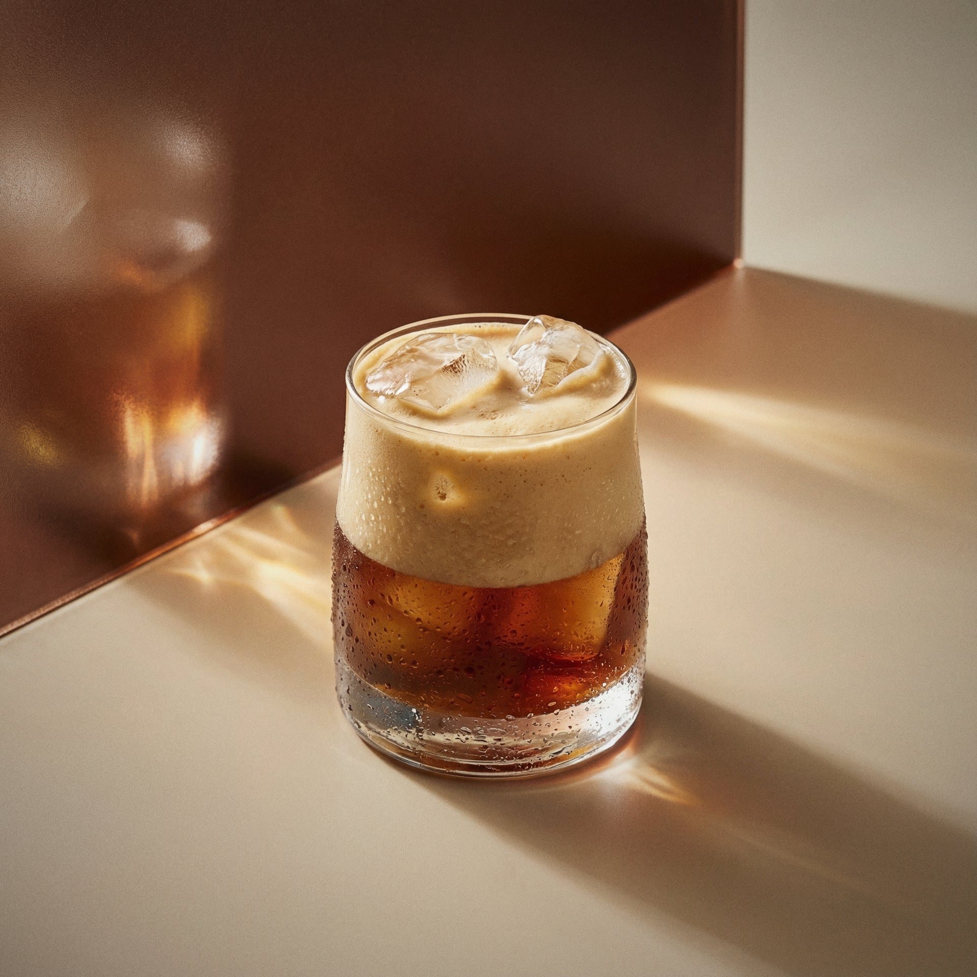 White Russian cocktail with coffee liqueur and vodka in a rocks glass with a creamy layer on a beige surface