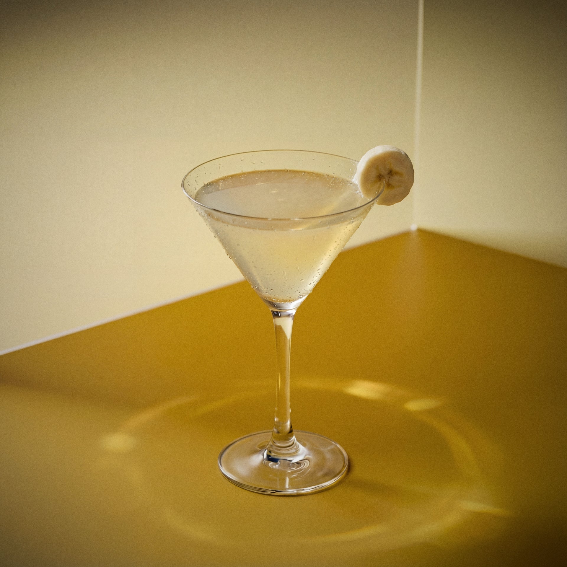 yellowbird Cocktail in a martini glass with banana liqueur, and a banana slice on a yellow surface