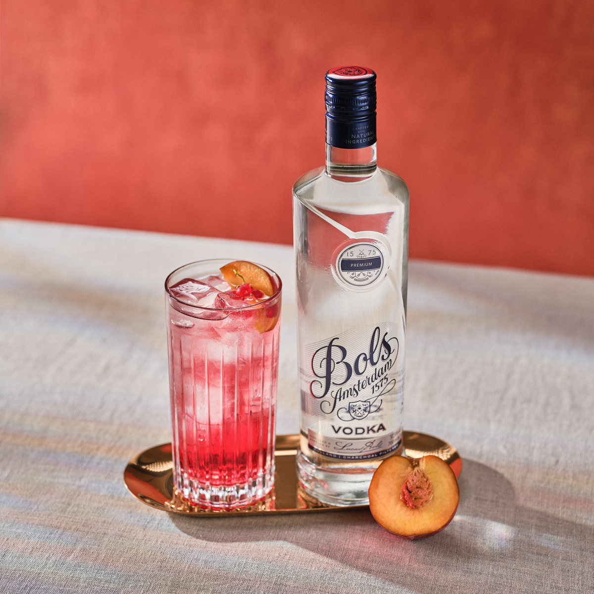 Bols vodka bottle with a cocktail and peach on a tray against an orange background